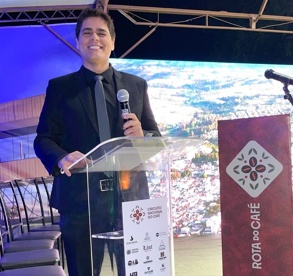 Matheus Pissolatti discursando em um púlpito de acrílico durante um evento corporativo